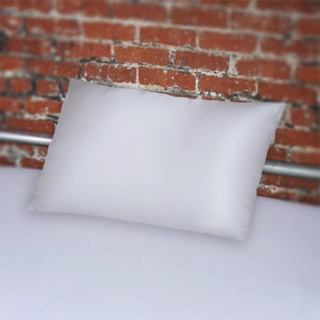 White fluidproof pillowcase on bed with silver frame against brick wall